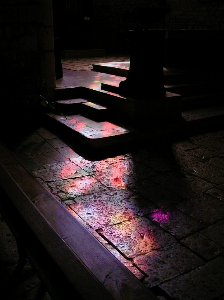 From darkness into Light--light from a stained-glass window on the dark stone floor of a medieval church in France.